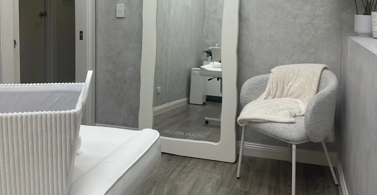 The full-length studio mirror beside a cushioned chair and treatment bed
