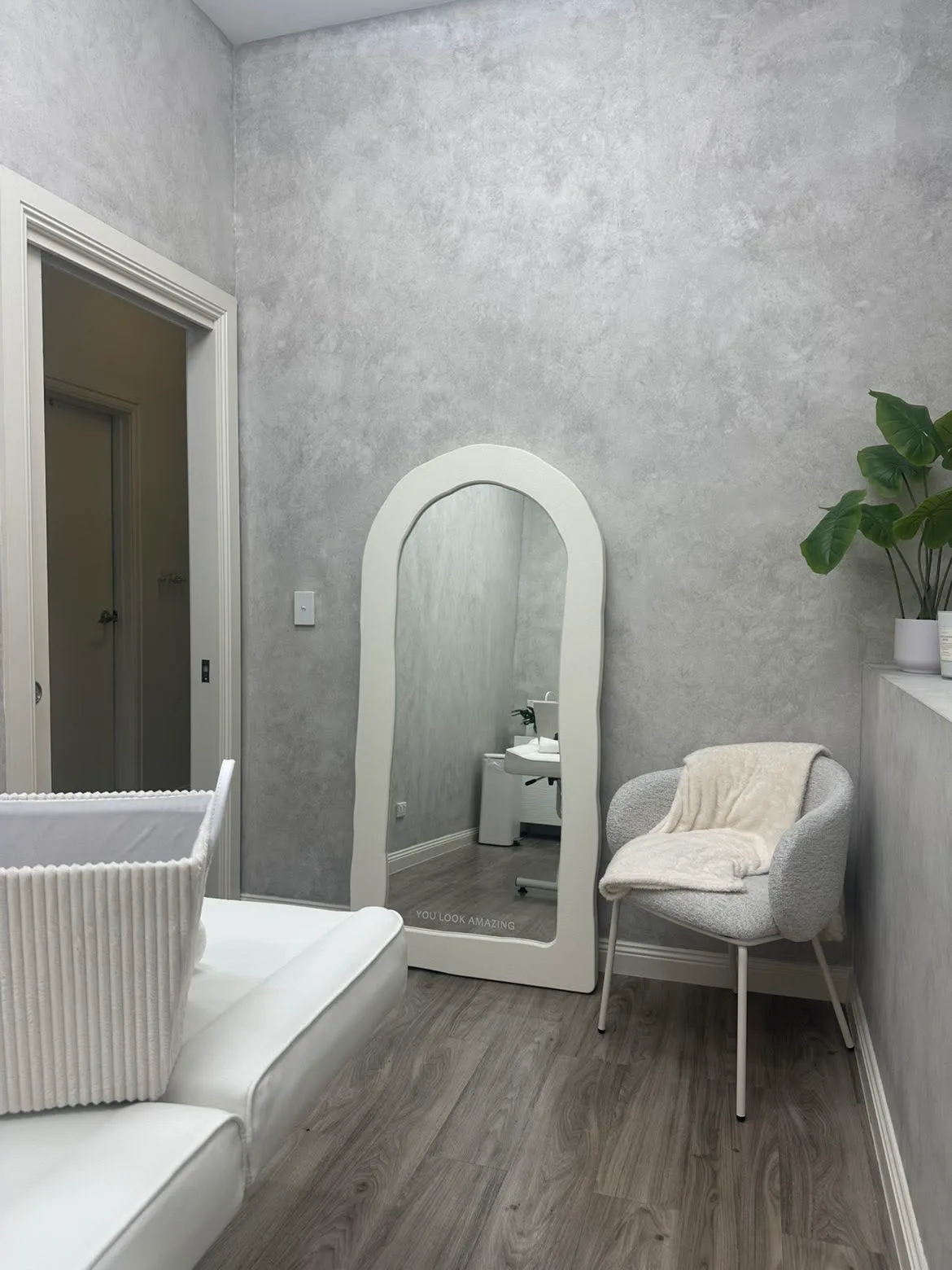 Arched white mirror reading You look amazing, beside a soft grey chair in the calm Luxe Laser Studio treatment room